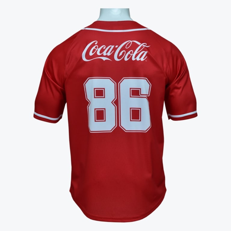 Back view of a red baseball jersey with the white Coca-Cola logo and the number 86 printed on it.