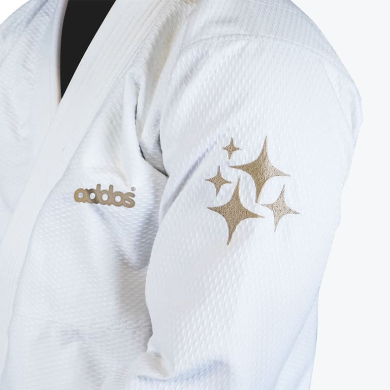 Close-up of a white Addos martial arts gi featuring gold embroidered stars on the sleeve and the Addos logo on the chest.