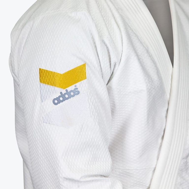 Close-up of a white martial arts gi sleeve with an embroidered Addos logo patch featuring a yellow chevron.