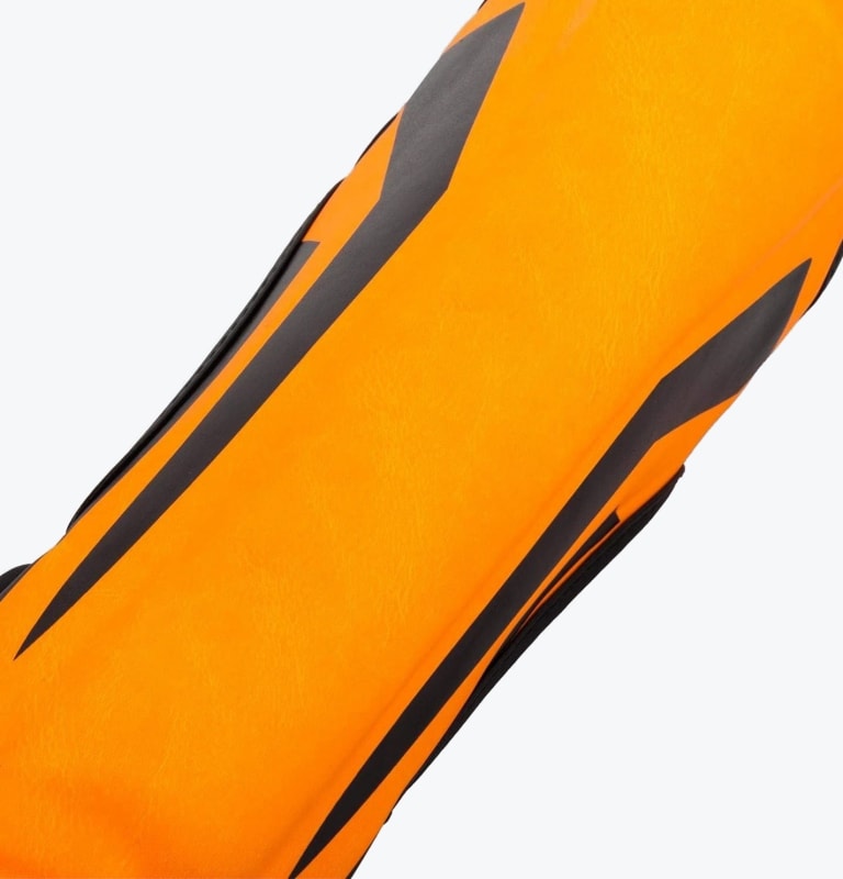 A close-up of a bright orange shin guard or sports sleeve featuring bold black geometric designs on a white background.