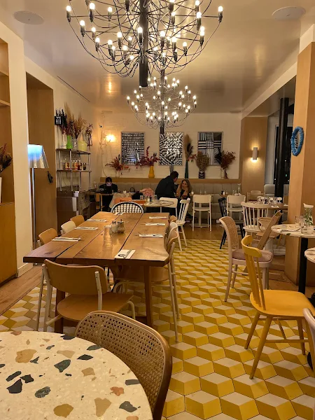 détails de la salle du Clint dans le 12ème arrondissement montrant une grande table en bois accueillante, une petite table en terrazzo, et au fond, une banquette occupée par des clients