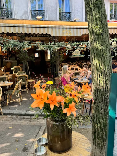 The terrace at Café Bohème in the background, behind a bunch of orange flowers. A cozy, bohemian space to learn French in Paris