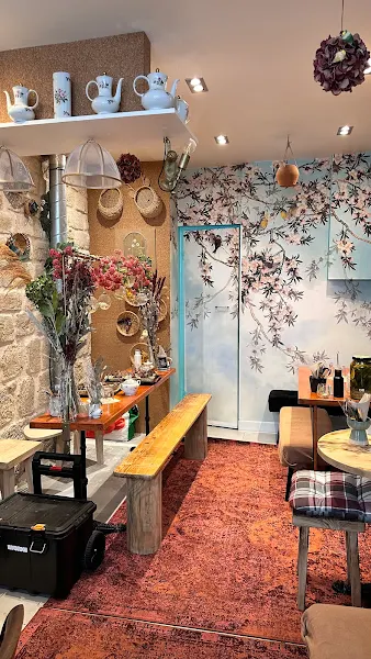 Interior view of La Cantine de Sam, with wooden tables, green plants, a red rug... In a bohemian, Montmartre style