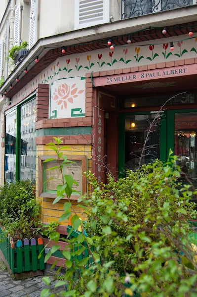 Exterior view of L'Été en Pente Douce, with colorful tables and green plants, a welcoming Montmartre vibe
