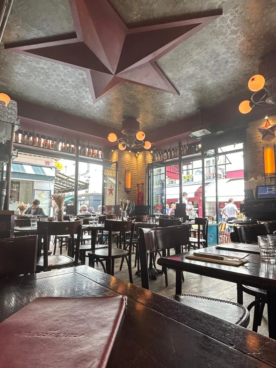 Intérieur du café du centre avec de grandes baies qui s'ouvrent sur des rues piétonnes. À l'intérieur des tables en bois, attendent qu'un client s'y installe.