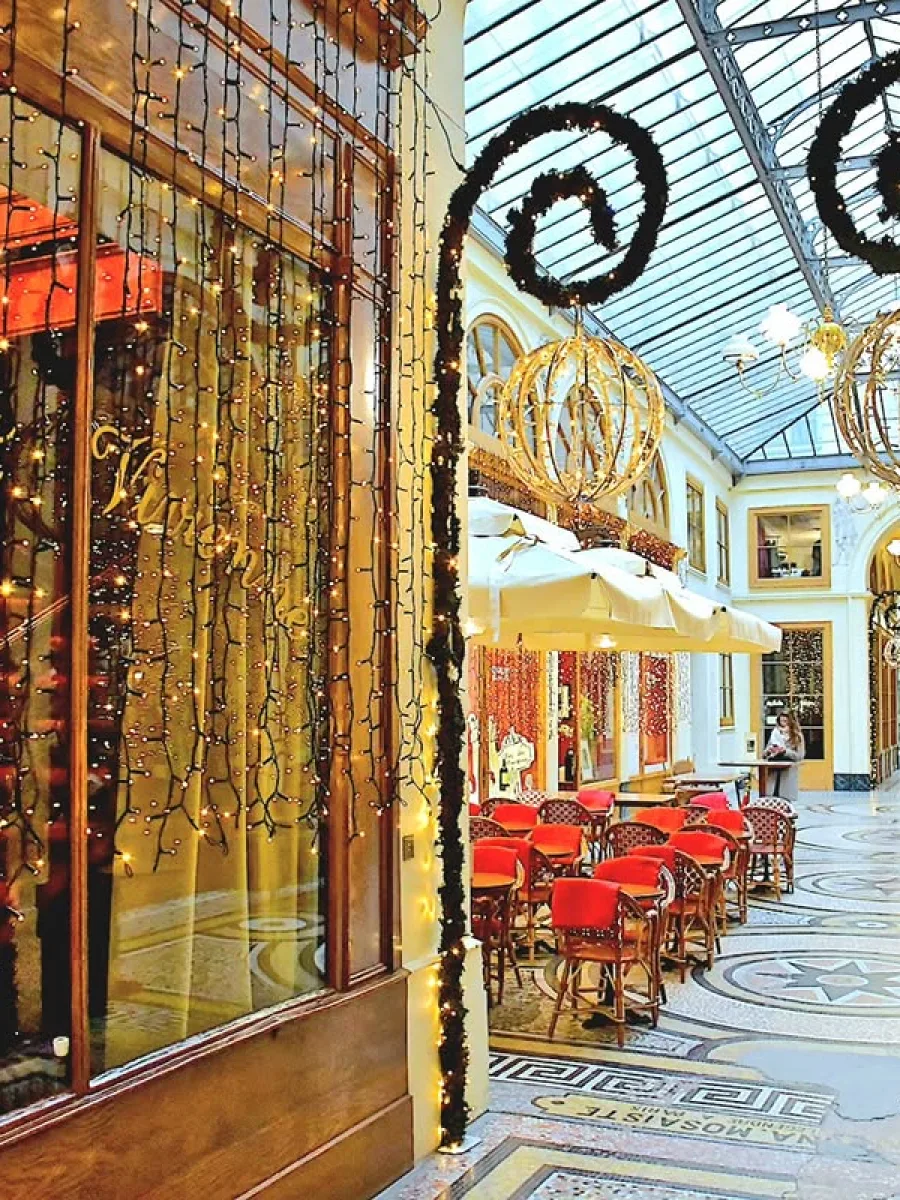 Devanture du bistrot Vivienne avec la terrasse en arrière-plan avec des tables, des couvertures sur le parterre de mosaïque de la galerie Vivienne.