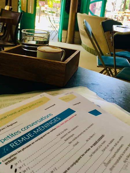 Prise de vue à l'intérieur du café Le Floréal avec nos supports de cours de français en premier plan et un café fumant à côté
