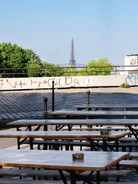 Prise de vue depuis la terrasse du café Moncœur Belleville avec vue sur la tour Eiffel et les tables en bois disposées sur la terrasse pavée