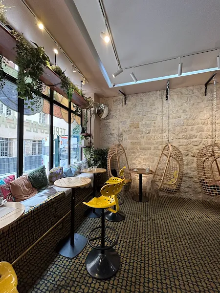 Intérieur cosy du café Terres de Café, avec des chaises jaunes, des balancelles en bois, une grande baie vitrée donnée sur l'extérieur.