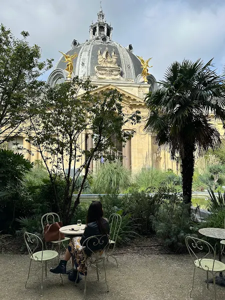 Vue de dos d'une étudiante en français langue étrangère assise à une table en fer forgé du Café 1902, dans le jardin du Petit Palais à Paris 8