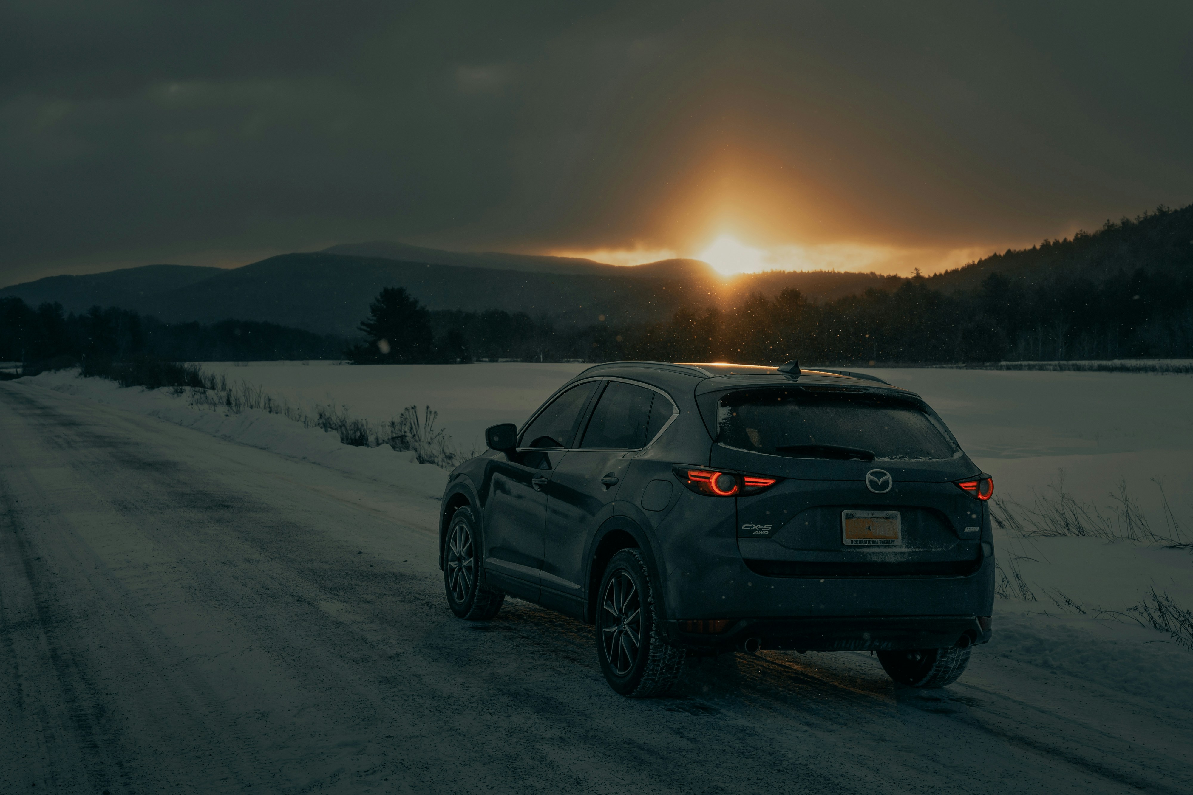 an SUV on a snowy road in front of mountains at dusk