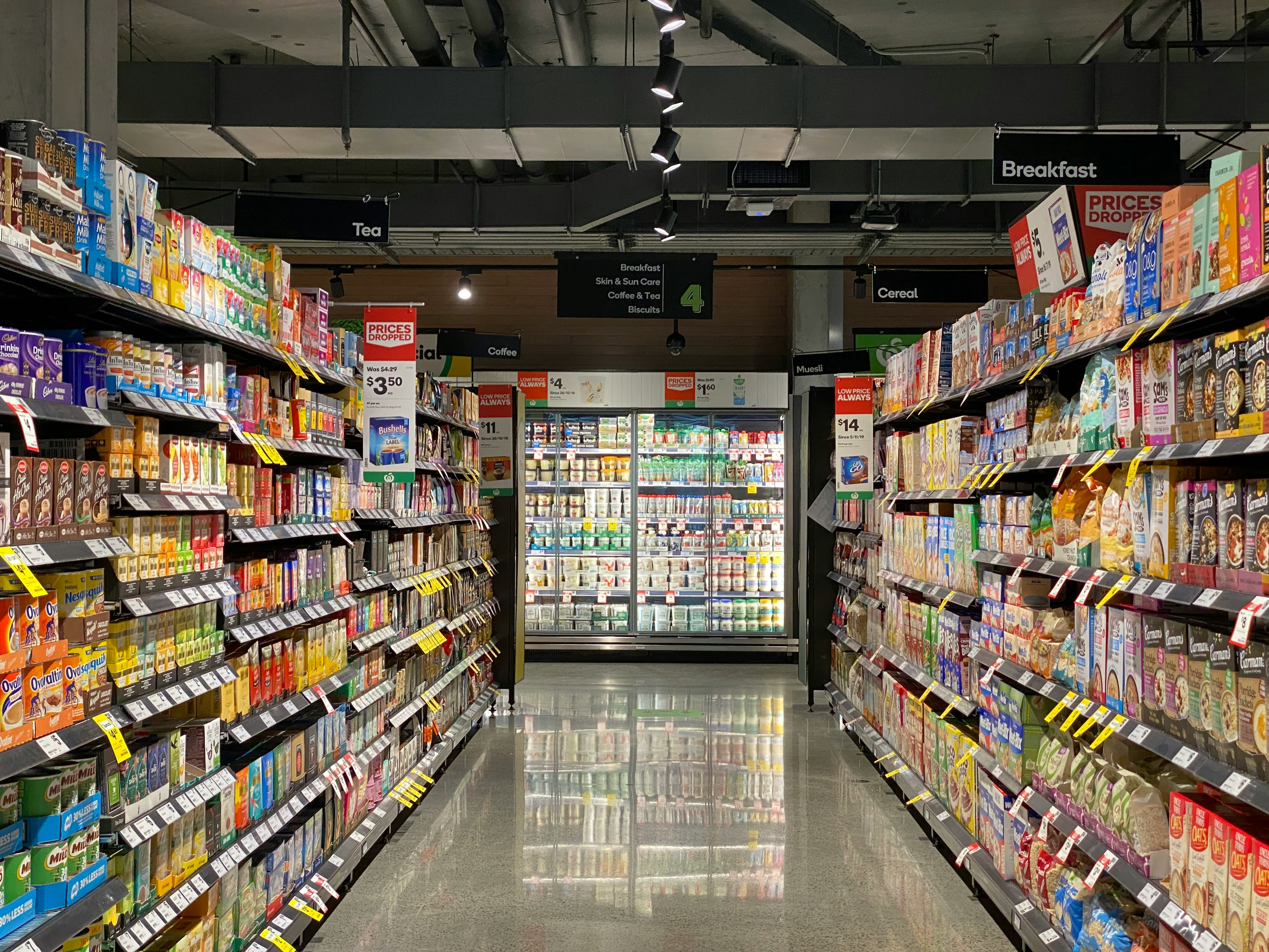 grocery aisle of breakfast cereals and pantry items with concrete floor and dairy fridge at end of aisle