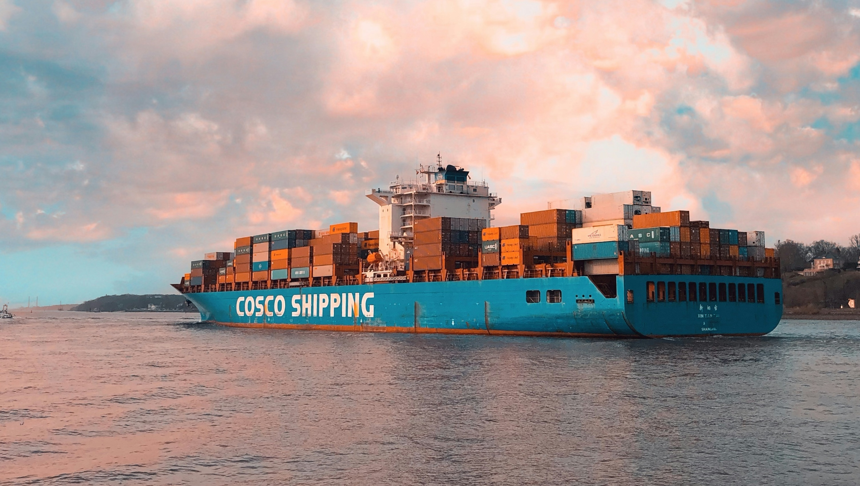 a blue freight ship on calm waters carrying stacks of shipping containers