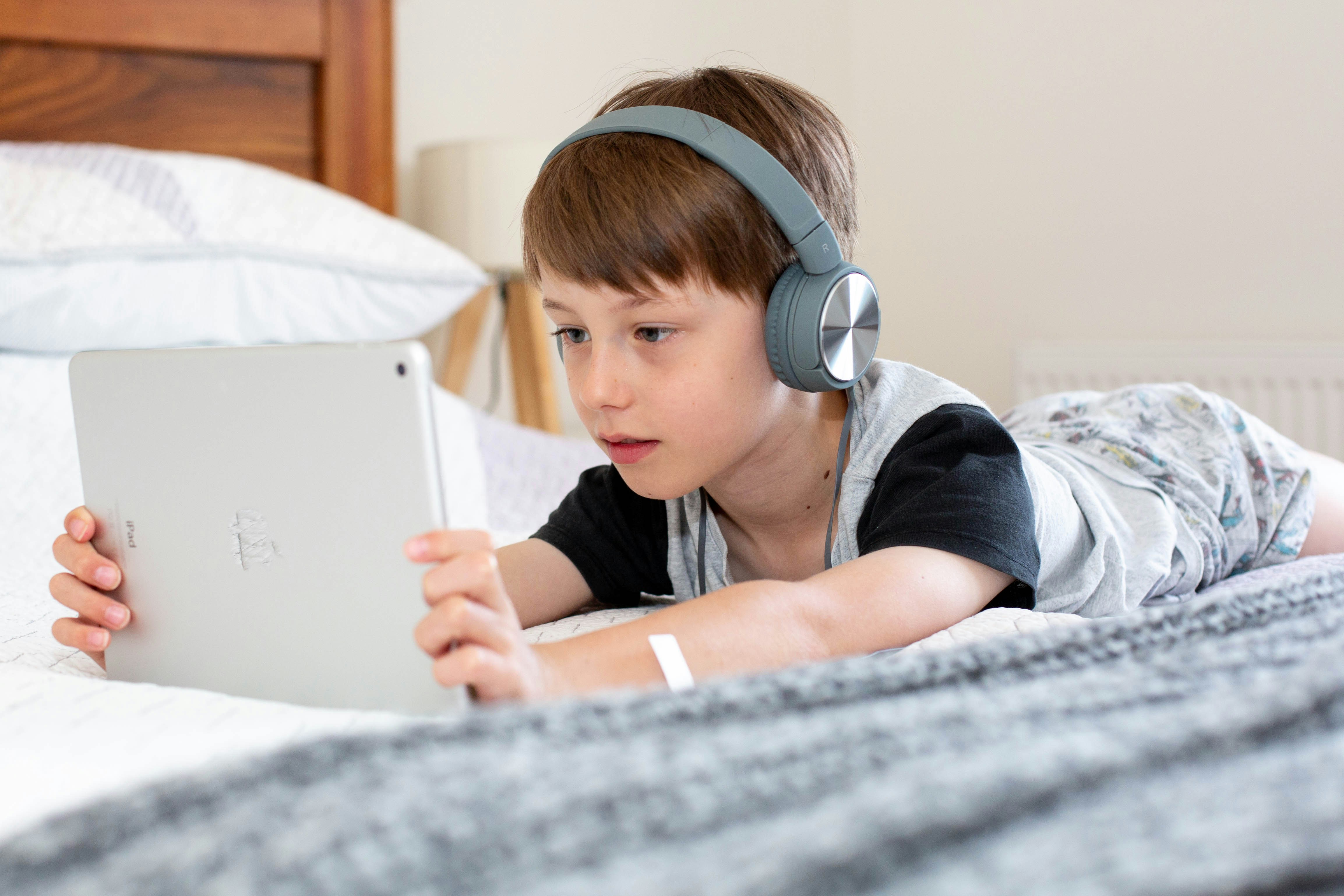 boy on bed wearing headphones watching iPad