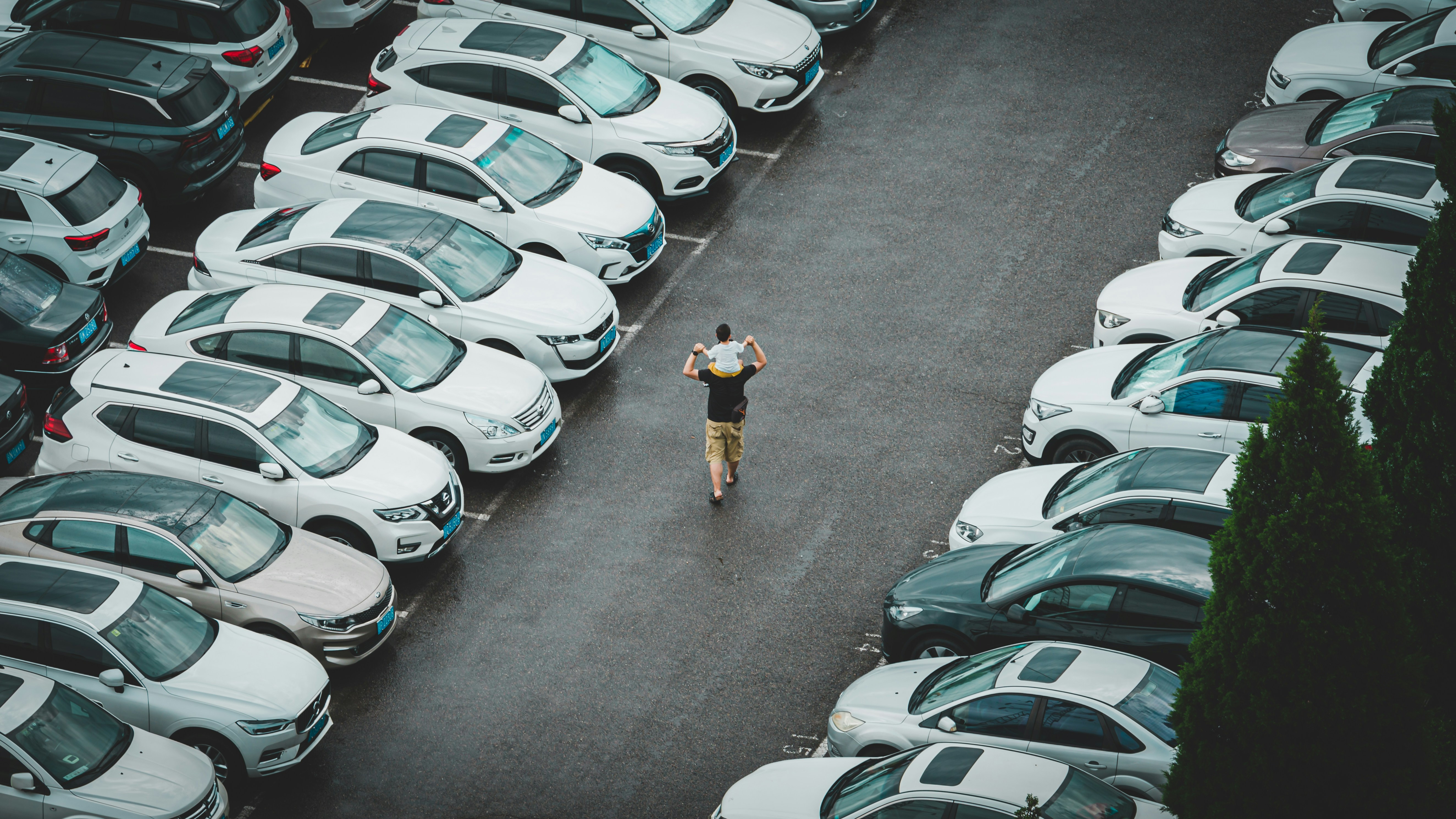 man with boy on shoulders walking through car lot from above