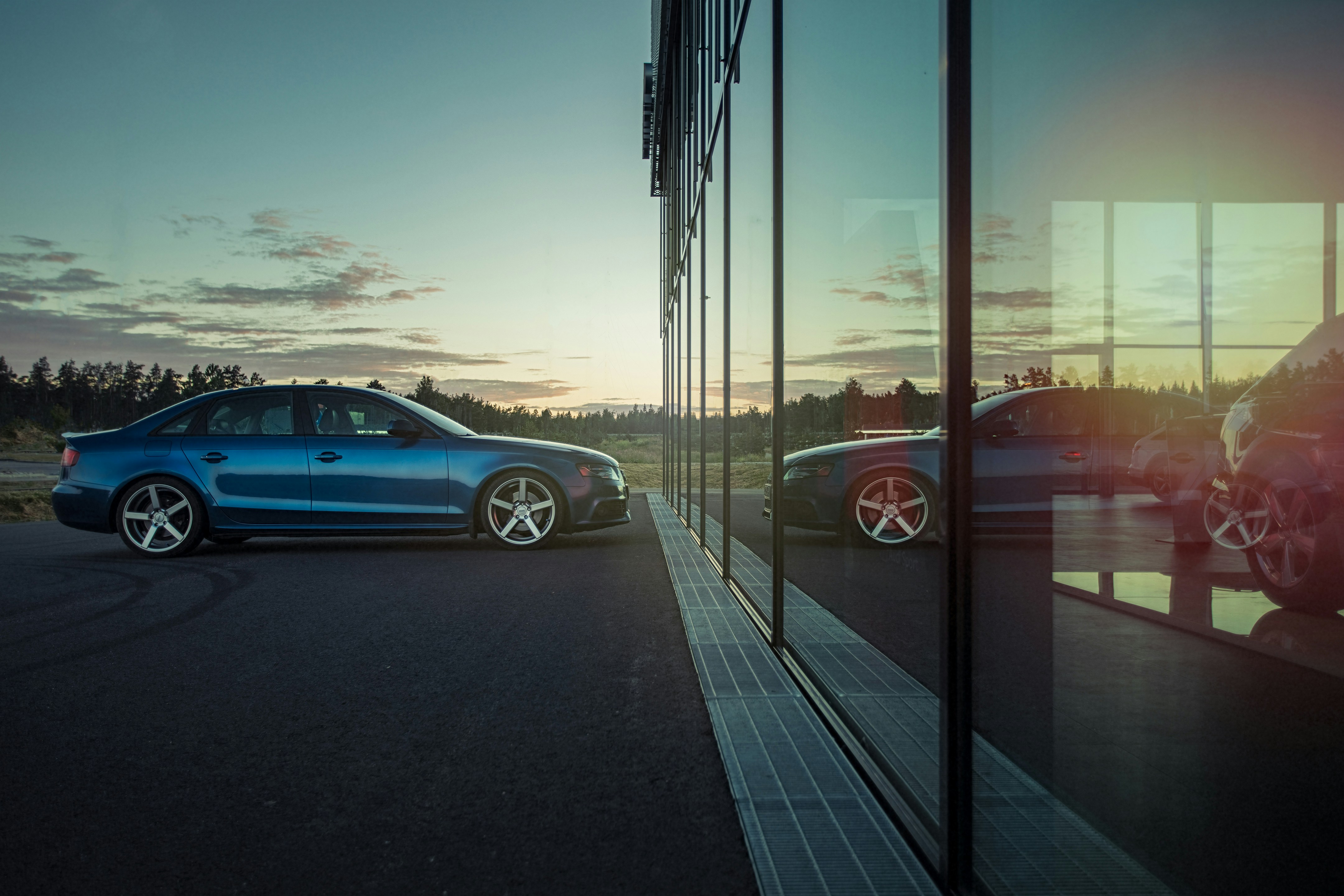 blue car in front of forest next to dealership, reflected in windows