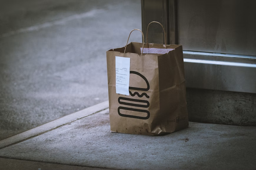 Takeout bag with burger and receipt on sidewalk