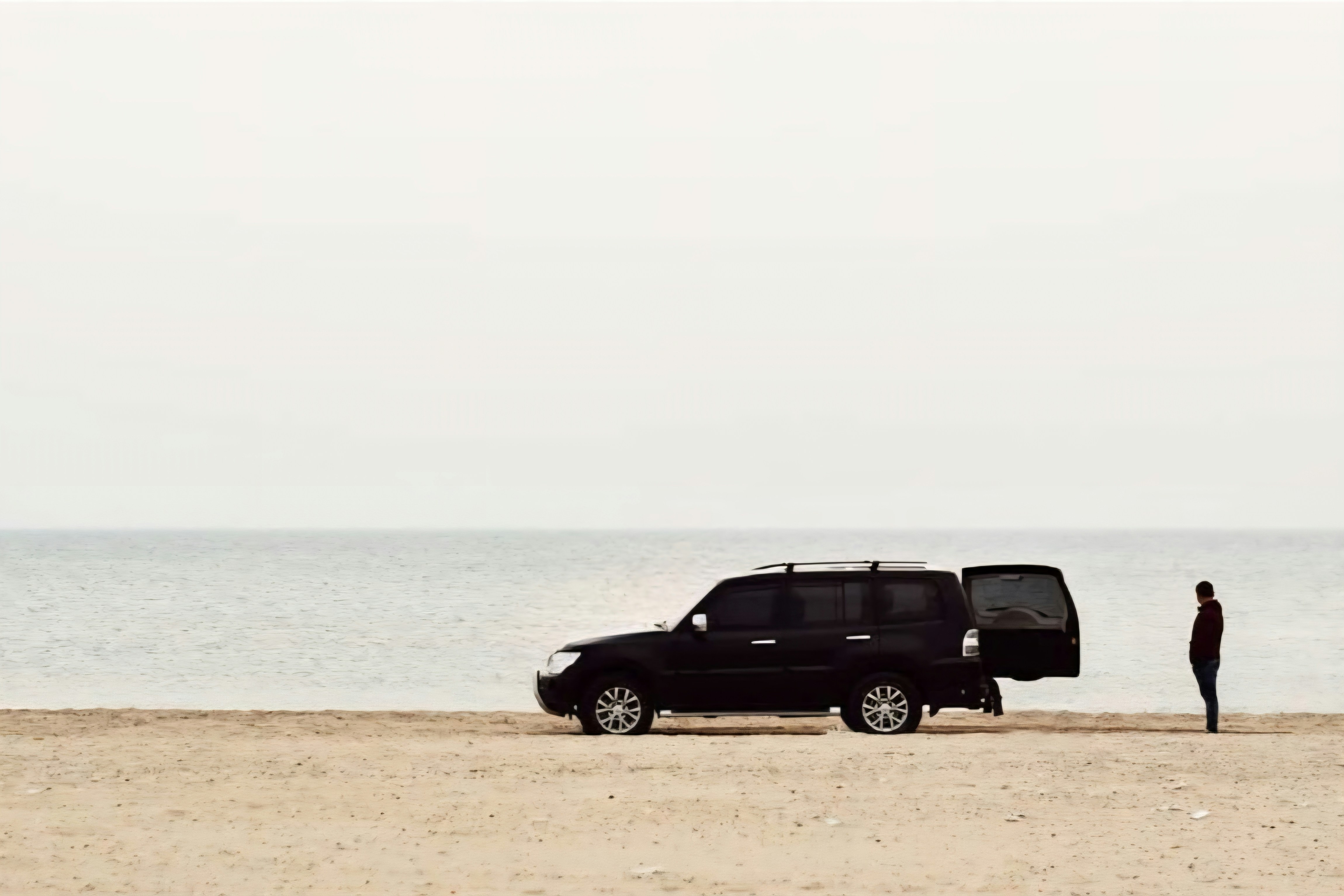 man on beach next to black SUV
