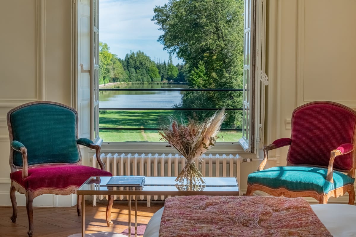 Fauteuils de velours devant une fenêtre ouverte sur l'étang dans une chambre de La Borde en Sologne