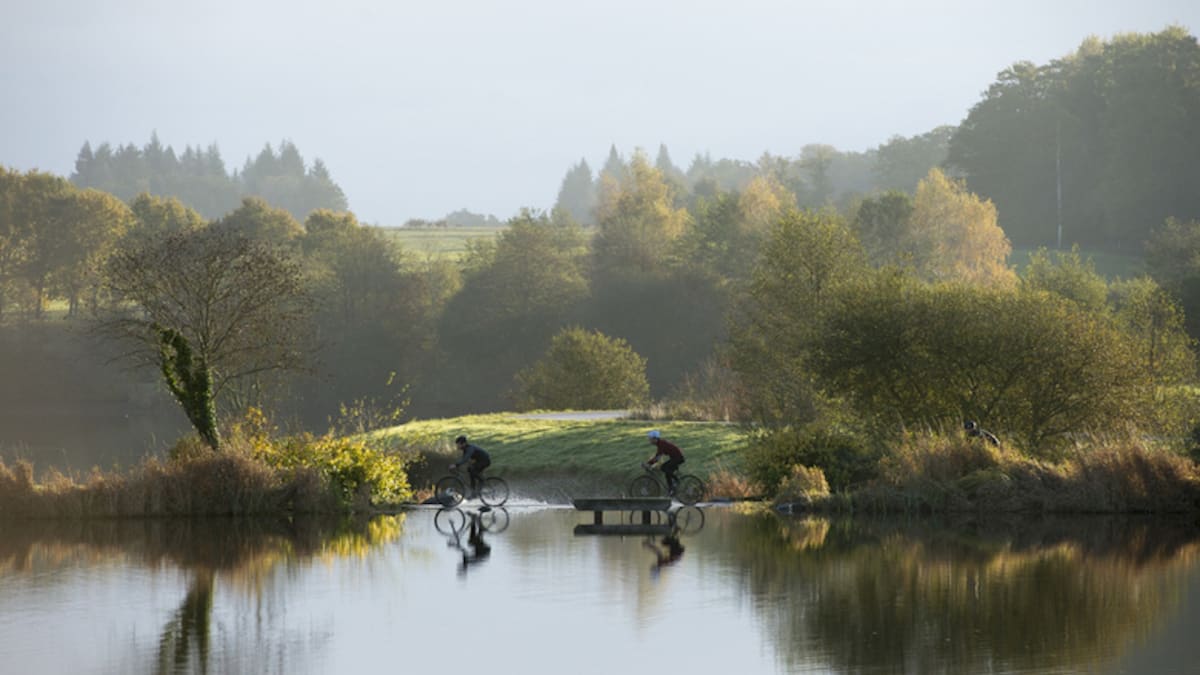 Deux cyclistes longent un étang dans la brume du matin au Domaine des Étangs, à Massignac en Charente