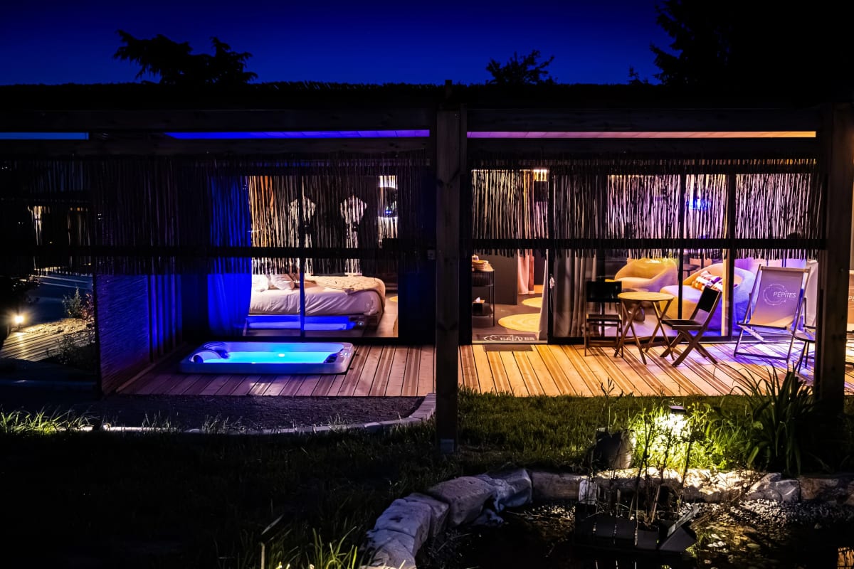 Lodge Pépites Lodges & Spas illuminé la nuit, baies vitrées ouvertes sur la terrasse et le spa privatif