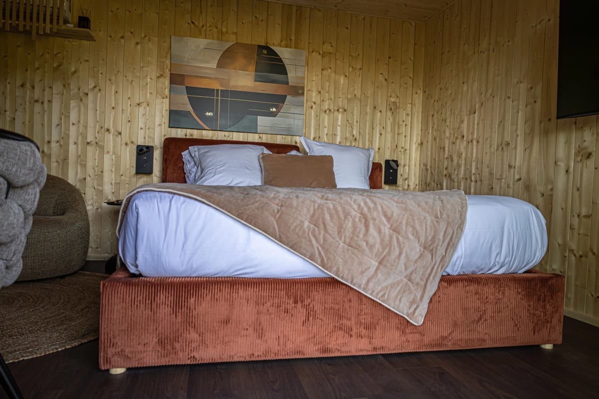 Chambre d'un lodge Pépites Lodges & Spas, murs en bois clair, grand lit et tête de lit en velours terracotta