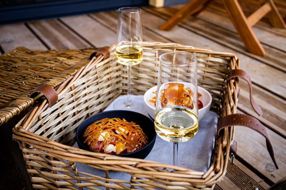 Panier en osier avec deux verres de vin blanc et un plat servi sur la terrasse d'un lodge Pépites Lodges & Spas