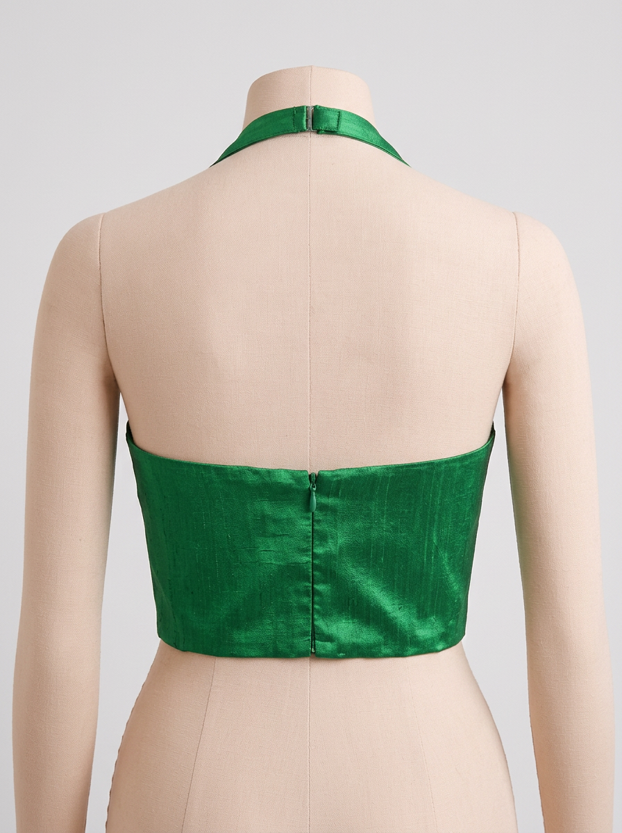 Back view of a green raw silk halter neck blouse on a mannequin, highlighting the concealed back zip closure and neck strap.