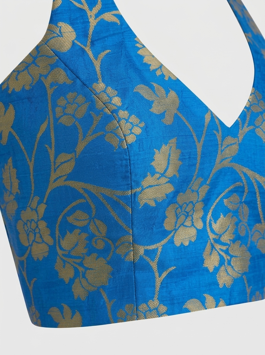 Close-up image of royal blue brocade fabric detailing intricate gold zari floral weaving and princess seam stitching.