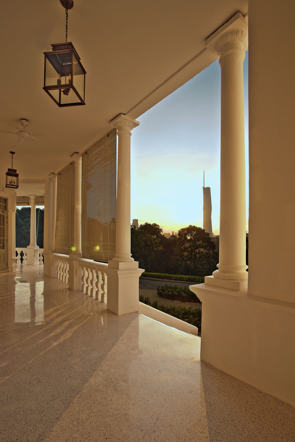 Restored Seri Negara verandah overlooking Kuala Lumpur skyline with classic white columns and polished terrazzo floor.