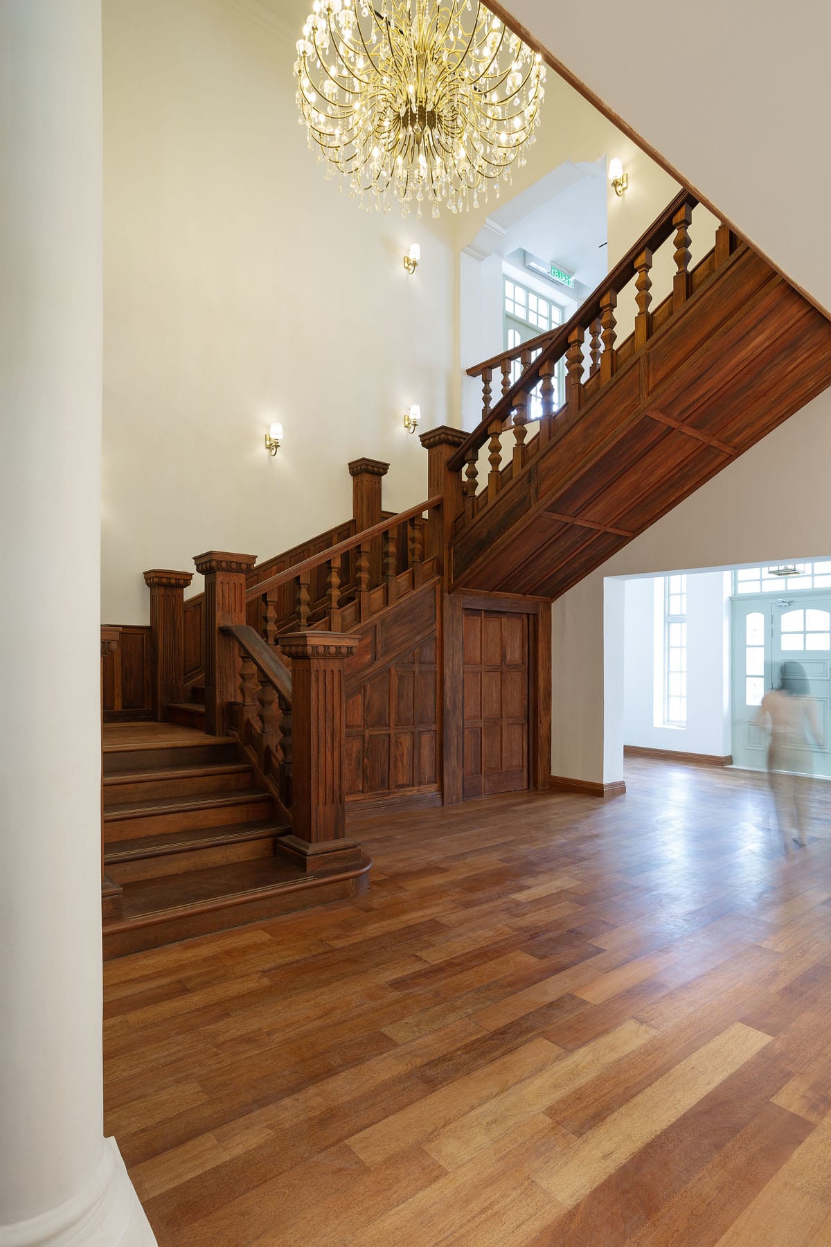 Restored grand wooden staircase, polished timber flooring, and chandelier inside Seri Negara heritage conservation project.
