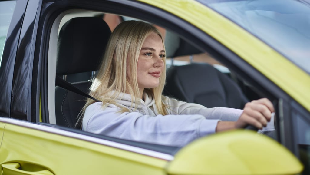 A young female driver looking happy behind the wheel of a green car