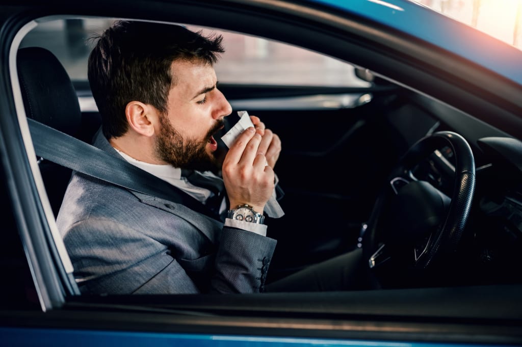 Male driver blowing his nose inside his car