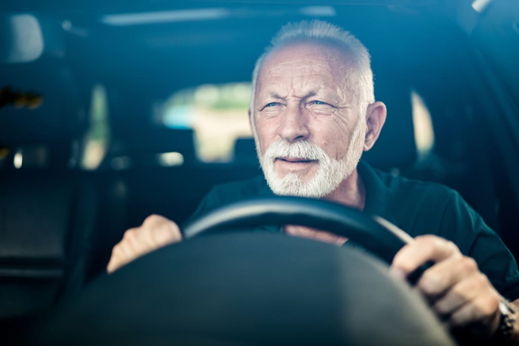 Senior man with white hair and beard gripping steering wheel, focused while driving