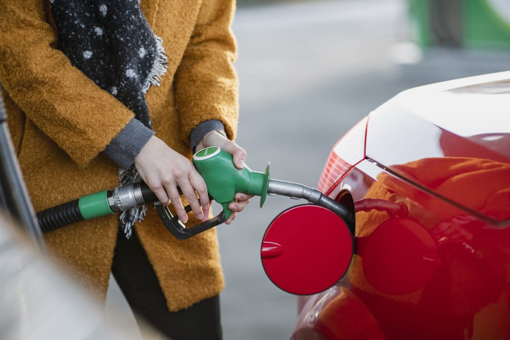 A person in a scarf and winter coat filling a car up with unleaded petrol from a petrol pump.