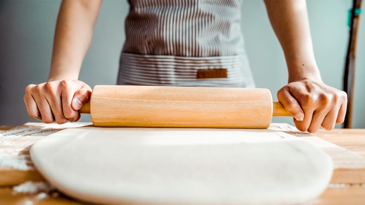 Gigpro pastry cook wearing apron uniform and using rolling pin to roll dough