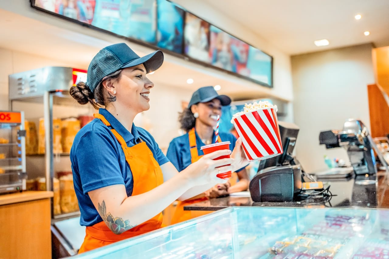 Two concession attendants serving popcorn and a drink at a venue counter