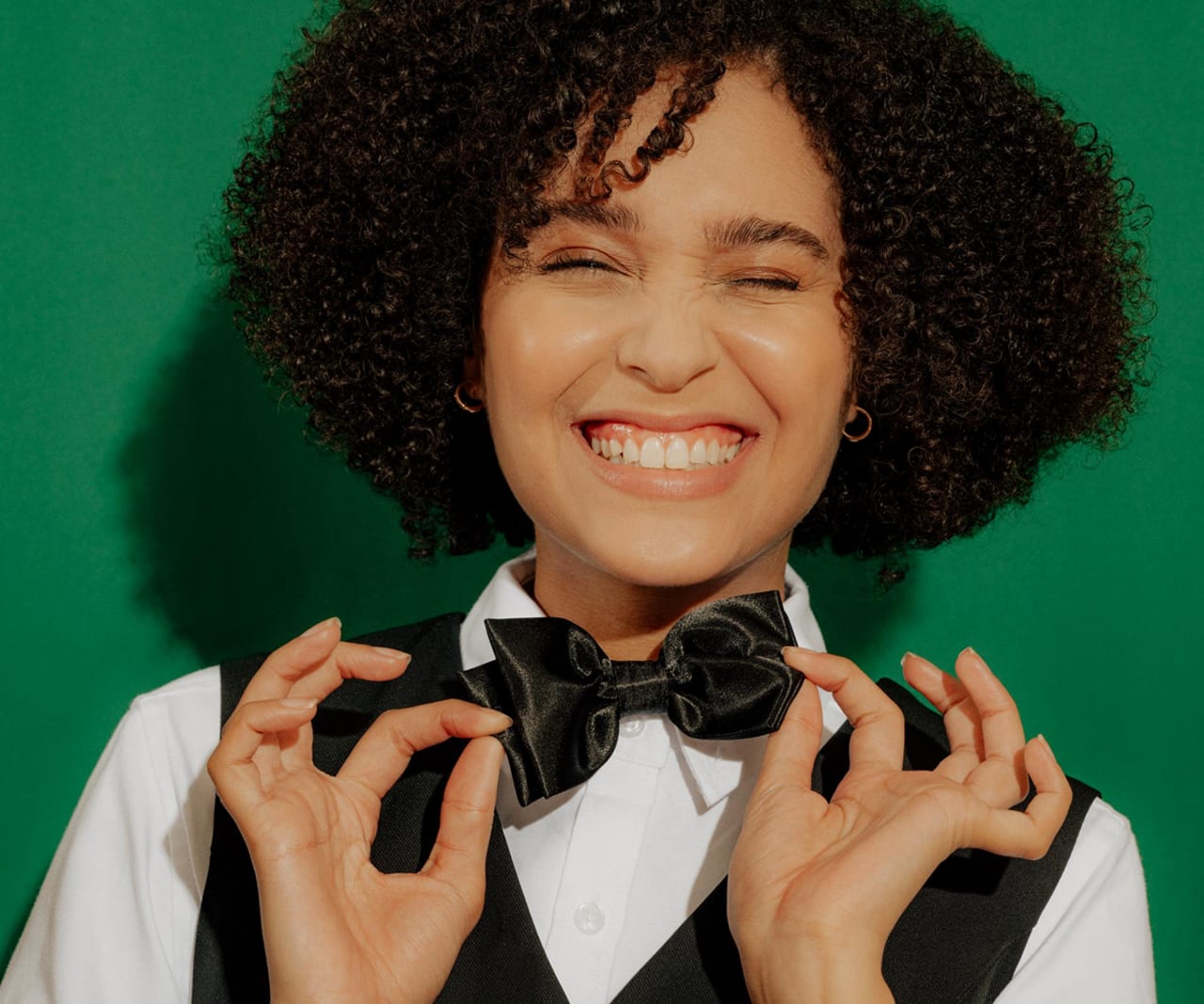 Smiling hospitality worker in a vest adjusting their bow tie