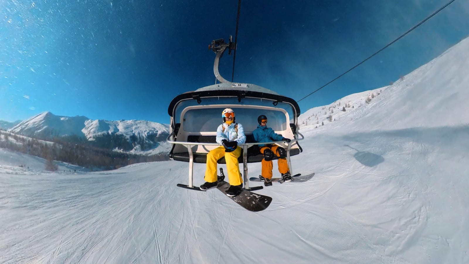 Two snowboarders on a chairlift in Livigno under a blue sky