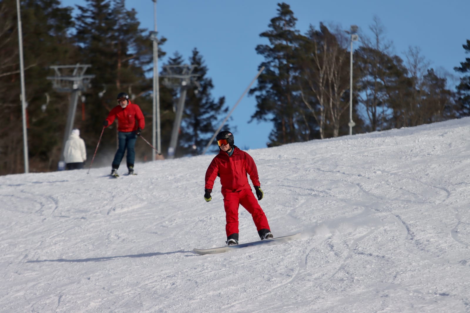 A snowboarder in a red suit riding a sunny slope near Jönköping, Sweden