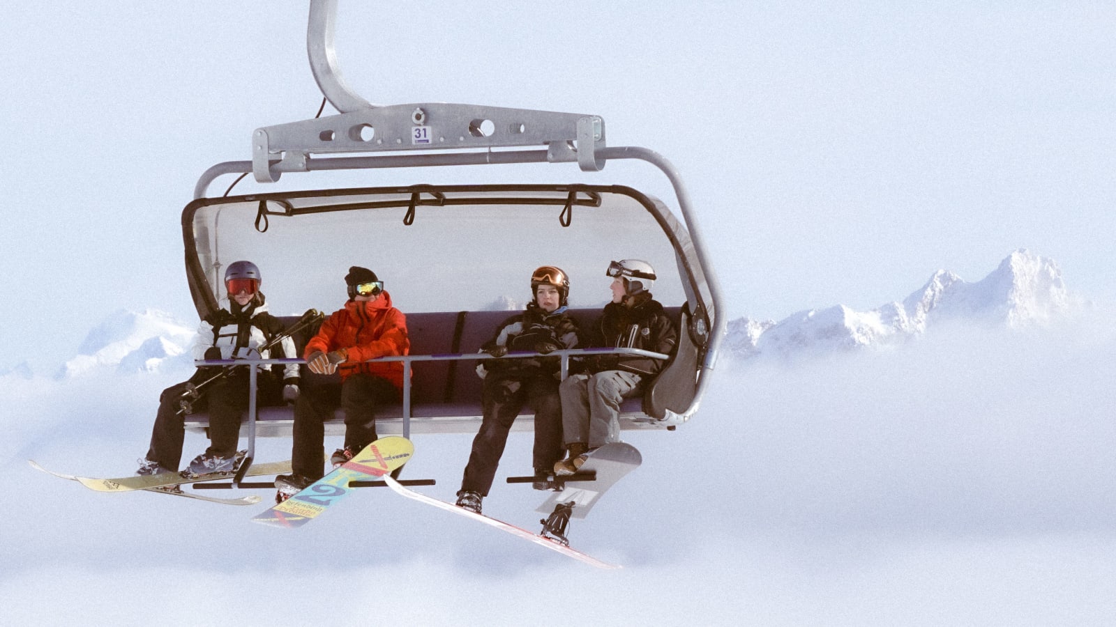 Four skiers and snowboarders on a chairlift above the snowy Alps