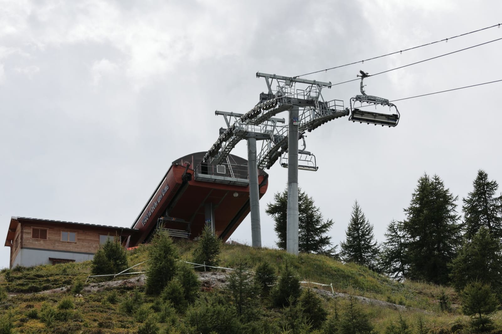 Ski lift station on a cloudy day in Puy-Saint-Vincent, France, surrounded by trees and grassy hills.