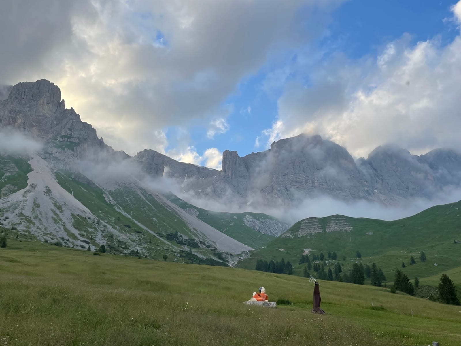 Serene meadow view of dramatic mountains in Moena, Italy, under a cloudy sky.