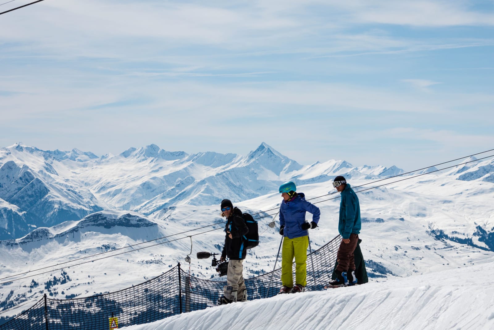 Three skiers on a snowy ridge in Laax with the Swiss Alps behind