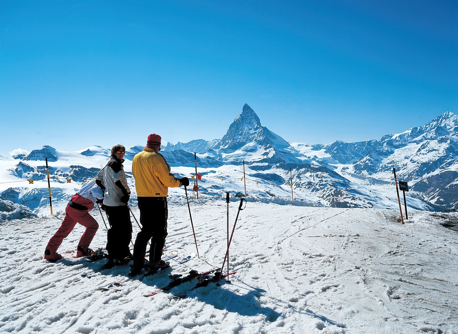 Three skiers on a snowy ridge looking towards the Matterhorn