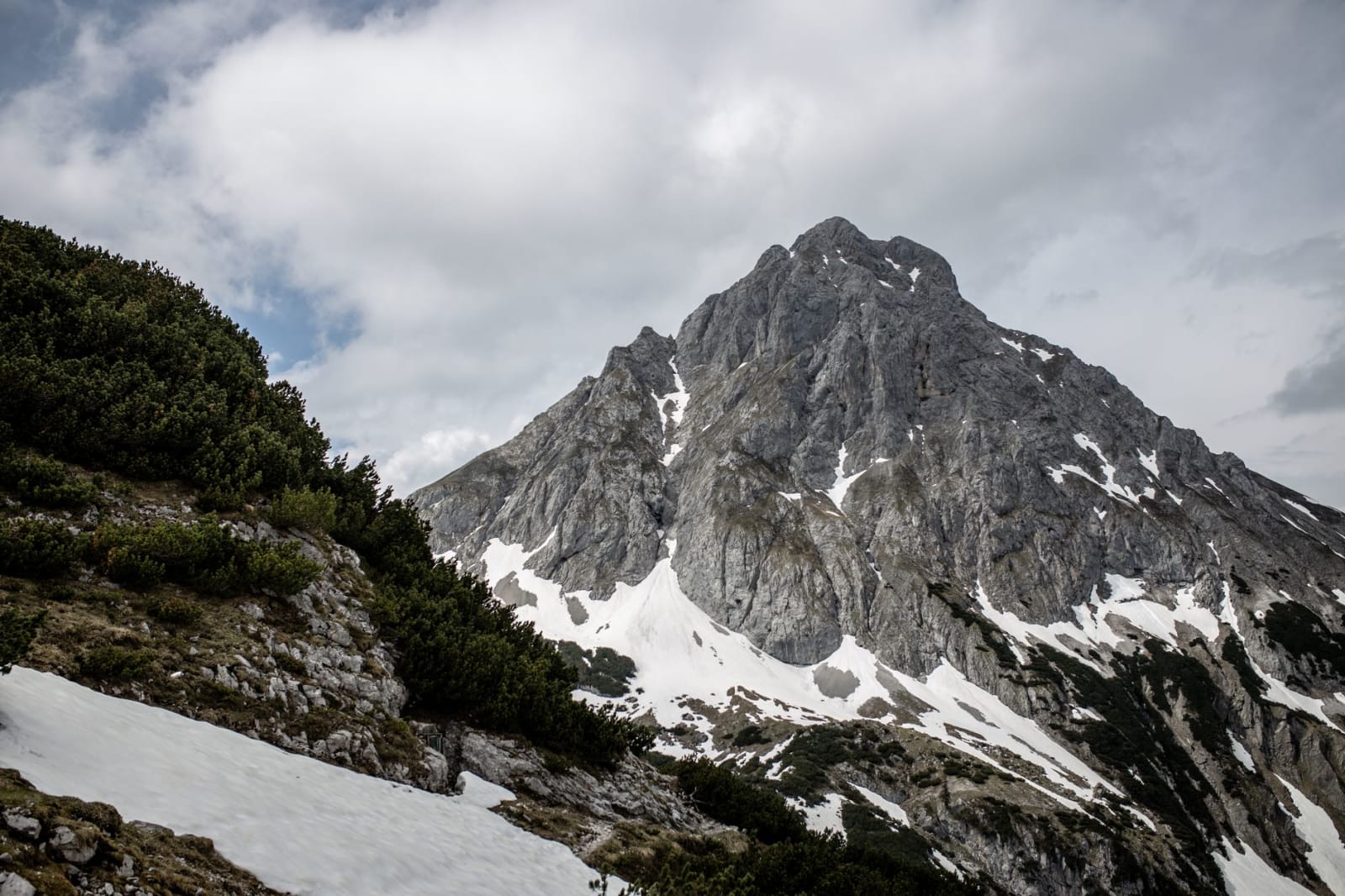 Scenic view of the snow-capped Ehrwalder Sonnenspitze, a rocky mountain in Austria under cloudy skies.