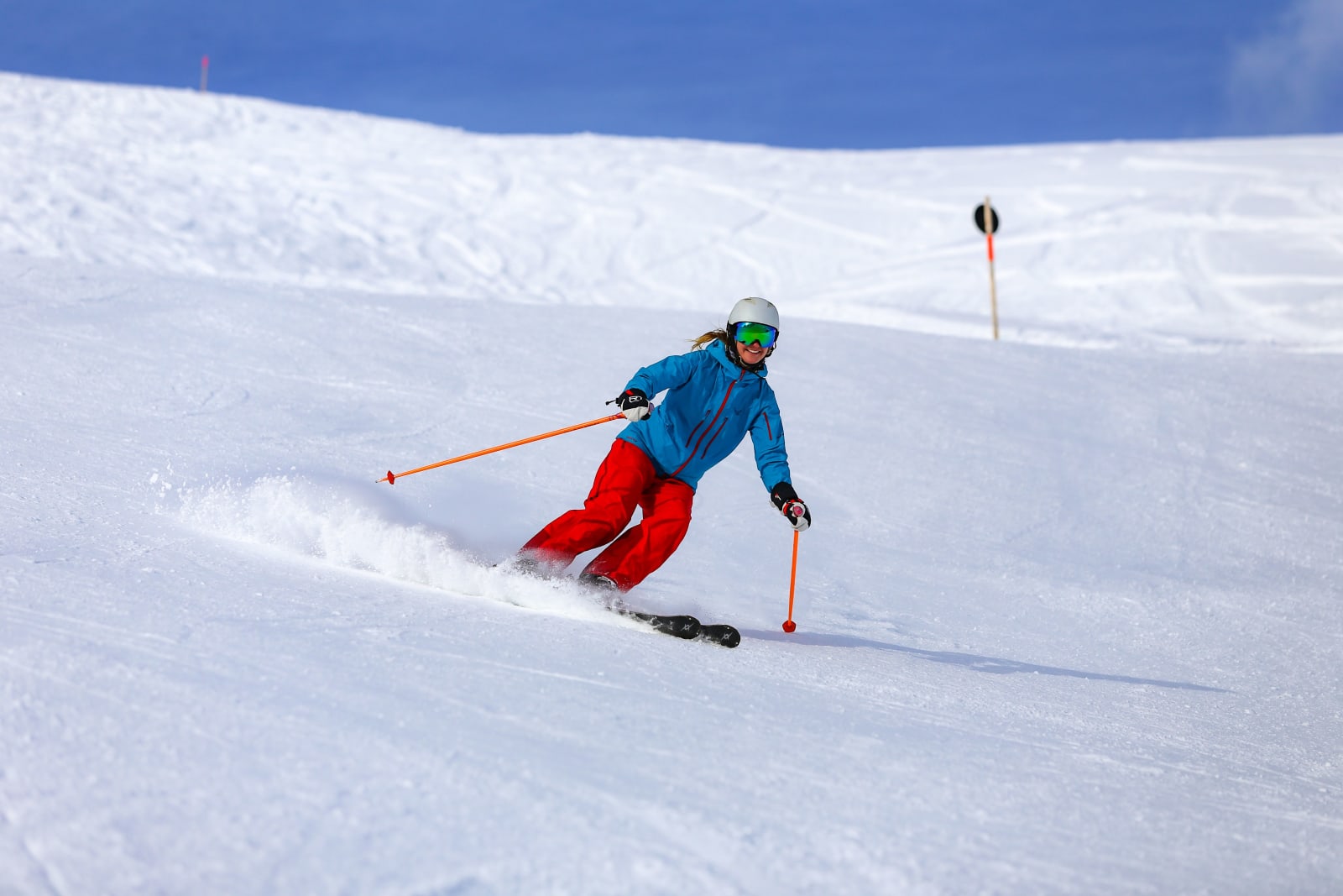 A skier in a blue jacket and red trousers carving a groomed slope in Vorarlberg