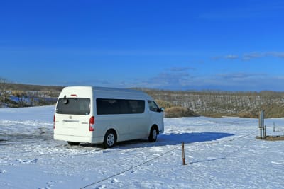 A solitary white van parked on a snow-covered landscape during a sunny day.