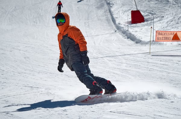 A snowboarder in an orange jacket carving a piste