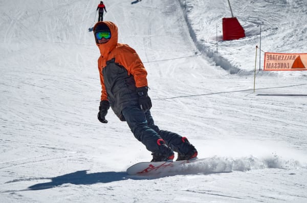 Snowboarder in orange jacket performing a carve on a snowy piste during winter.